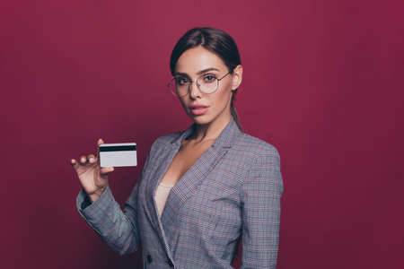 Portrait of her she nice cute attractive lovely chic gorgeous confident lady gray checked jacket holding in hands showing plastic card balance budget isolated over maroon burgundy marsala backgroundの写真素材