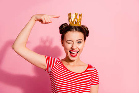 Close-up portrait of her she nice cute attractive lovely winsome gorgeous cheerful cheery glad flirty girl wearing striped t-shirt showing cool gold diadem isolated over pink pastel backgroundの写真素材