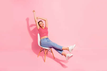 Nice-looking attractive winsome lovely adorable cheerful girl wearing striped tshirt jeans lying on chair resting having fun spare time pleasant isolated over pink pastel backgroundの写真素材