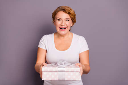 Portrait of her she nice attractive cheerful cheery girlish wavy-haired lady in casual white t-shirt holding in hands desirable box isolated on gray violet purple pastel backgroundの写真素材