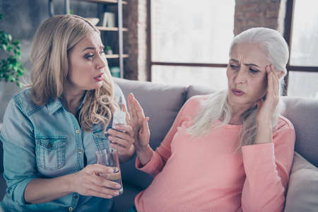 Close up photo two people she her ladies granddaughter bring medicine difficult health condition do not want take pills granny hold hands arms temples suffer head ache couch divan sofa house indoorsの写真素材