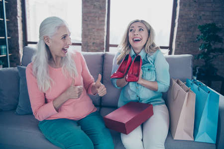 Close up photo two funny beautiful people models she her ladies granny granddaughter showing new collection red fashion high-heels got tips thumb up good choice sit couch divan sofa house indoorsの写真素材