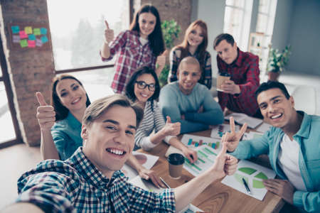 Self-portrait of nice stylish attractive cheerful business sharks finance managers company team-building showing thumbup v-sign at industrial interior workplace workstationの写真素材
