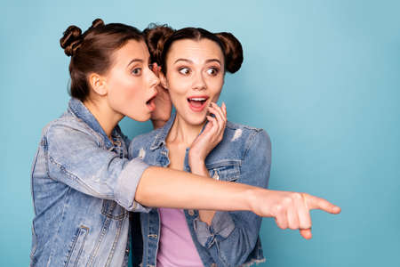 Look thats unbelievable. Portrait of shocked impressed ladies looking at advertisement advising choosing deciding selecting noticing presenting news information in denim jackets on blue backgroundの写真素材