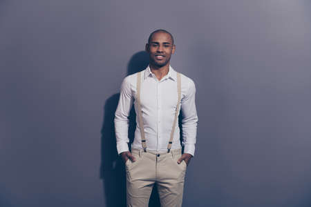 Close up photo beautiful amazing funky dark skin he him his macho arms pockets look easy-going kind sincere eyes shiny shaved face wear pastel pants suspenders white shirt isolated grey backgroundの写真素材