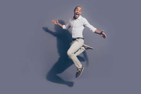Full length side profile body size photo amazing dark skin he him his macho jumping high great mood childish playful crazy fooling around wear white shirt pastel pants isolated grey backgroundの写真素材