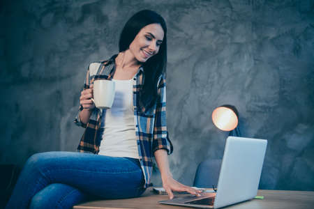 Portrait of nice cute attractive charming cheerful brunette lady wearing checked shirt free time browsing news video chat sitting on desk at industrial loft style interior work place stationの写真素材