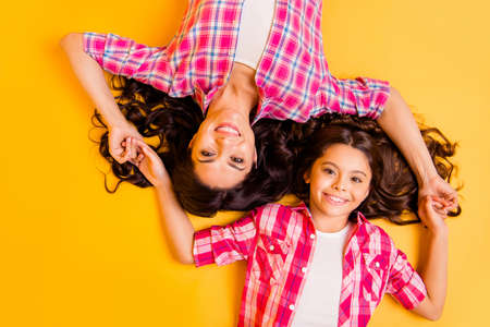 Close up top above high angle view photo beautiful she her models mom daughter caress arms together long hair weekend lying floor wear casual pink plaid checkered shirts isolated yellow backgroundの写真素材