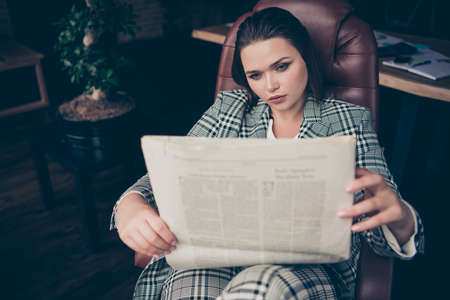 Close up photo amazing beautiful she her business busy lady hold arms hands newspaper look wondered marketing article sit big large office cozy chair wear formal-wear checkered plaid suitの写真素材