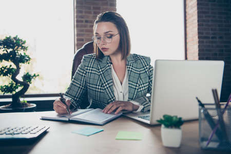 Close up photo beautiful she her business lady use user diary pen write notices look attentively counting payment notebook table sit office chair wearing specs formalwear checkered plaid suitの写真素材
