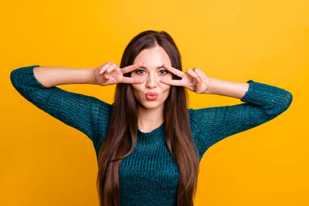 Close up photo funky beautiful her she lady arm hand fingers show v-sign near brown eyes send air kisses long straight hair wear jeans denim green knitted pullover jumper isolated yellow backgroundの写真素材