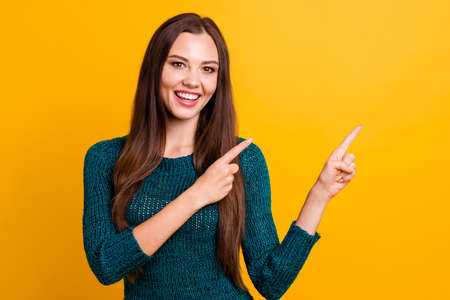Close up photo beautiful her she lady white teeth indicate arm finger empty space advising buy buyer new clothes prices long straight hair wear green knitted pullover jumper isolated yellow backgroundの写真素材