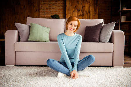 Close up photo amazing beautiful she her lady hand palm arm hold legs red short hairdo wear blue pullover jeans denim clothes sit floor fluffy carpet comfortable divan house loft living room indoorsの写真素材