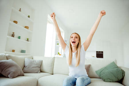 Portrait of funny funky charming lady sit divan raise fist feel satisfied cheerful delighted scream...