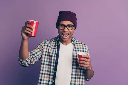 Photo portrait of crazy funky guy enjoying holiday weekend holding raising plastic glass with beverage in hand isolated violet backgroundの写真素材