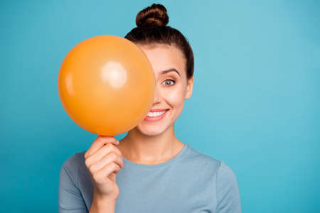 Close up photo of cute attractive lady hold hand orange ballons for anniversary hide feel content enjoy rejoice free time dressed cotton fashionable spring clothes isolated on blue backgroundの写真素材