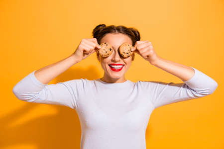 Portrait of cute charming attractive lady fooling around closing hiding her eyes with biscuits try to lose weight dressed in white cotton outfit isolated over vibrant backgroundの写真素材