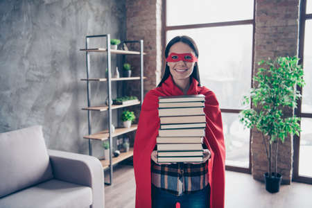 Close up photo beautiful she her superpower lady comics costume women equal rights concept strong hands arms hold many lot books wear red eye mask mantle house living room loft flat indoorsの写真素材