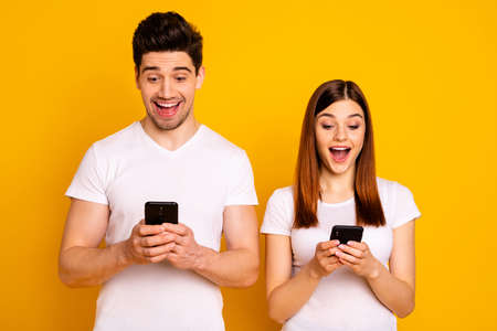 Portrait of his he her she two nice attractive charming stylish trendy cheerful cheery people using new cool chatting gadget device isolated over vivid shine bright yellow backgroundの写真素材