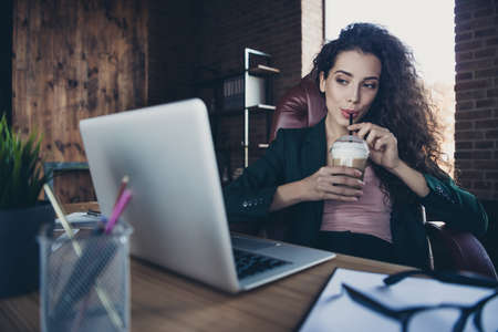 Close up photo of beautiful charming fabulous lady executive sit armchair have beverage mug look screen pc read information feel content wear black jacket hairstyle sit table in industrialの写真素材