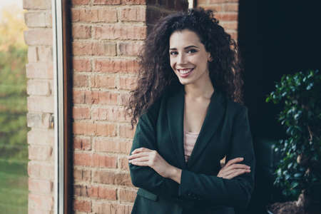 Portrait cute millennial charming freelancer content glad rejoice satisfied enjoy excited relaxed long wavy curly hair hairstyle stand window interior dressed modern stylish trendy classic jacketの写真素材