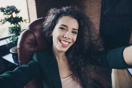 Close up photo of cute elegant entrepreneur chairman with long curly wavy hair hairstyle sit chair feel content candid make photos have leisure free time pause wear black blazers in loftの写真素材