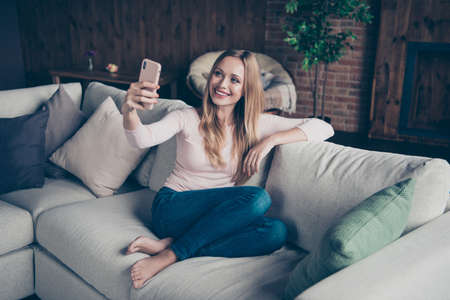 Photo portrait of attractive cheerful calm positive optimistic charming she her lady using telephone having blog sitting on divan without shoesの写真素材