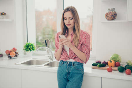 Close up photo beautiful amazing she her lady vegan hold hands arms telephone interested curious wondered homey wear domestic home apparel shirt jeans denim outfit bright flat home kitchen indoors.の写真素材