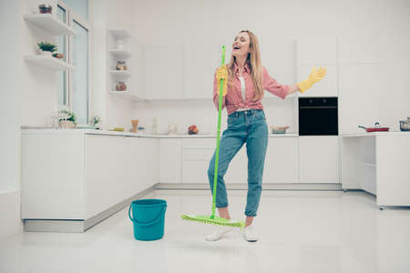 Full length body size photo beautiful busy nice duties she her lady wash white floor funky housemaid karaoke day singing mop crazy wear jeans denim casual plaid checkered shirt bright light kitchenの写真素材