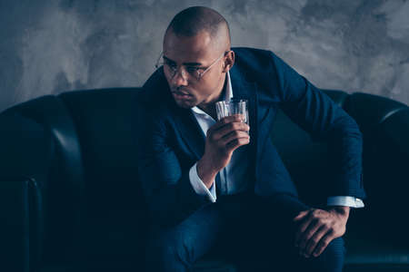Portrait of his he nice stylish trendy classy chic imposing elegant attractive guy wearing jacket top manager sitting on couch drinking beverage at work place station gray concrete wall.の写真素材