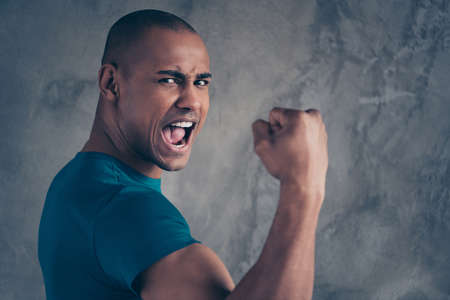 Close up side profile photo amazing he him his dark skin macho handsome hand arm fist raised best win yelling football fan match game goal score wear casual blue t-shirt isolated grey background.の写真素材