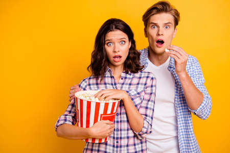 Close up photo of pair  he him his she her lady boy eyes wide opened pop corn in mouth close to each other afraid of horror film wearing casual plaid shirts outfit isolated on yellow backgroundの写真素材