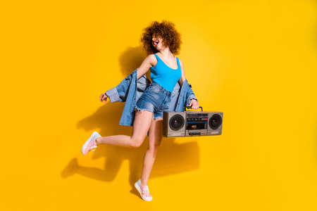 Full length body size photo beautiful she her lady wavy styling curls old-fashioned tape recorder dancing excited wear specs casual jeans denim shirt shorts tank top clothes isolated yellow backgroundの写真素材