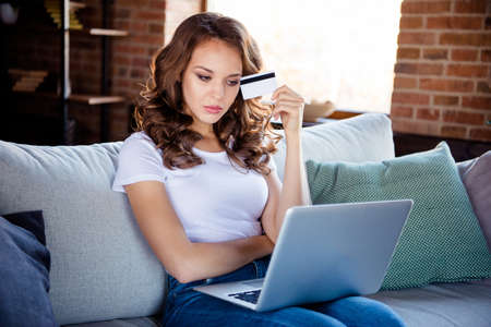 Portrait of her she nice attractive lovely serious wavy-haired girl sitting on comfortable divan holding in hand card buyer pay payment purchase at industrial loft wooden brick style interiorの写真素材