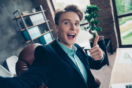 Portrait positive cheerful youth relax rest break pause video call make photo sit table desk advertise choose decide recommend excellent feedback jacket stylish trendy handsome industrial interior.の写真素材