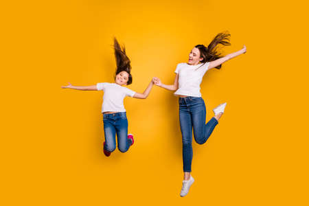 Full length body size photo beautiful her she diversity different age lady hold arms spend free time together jump high hair flight wear casual white t-shirts jeans denim isolated yellow backgroundの写真素材