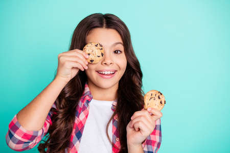 Portrait of funny funky cute pretty child have confectionery pastry hide face enjoy rejoice crazy content dressed checked shirt modern outfit isolated turquoise background.の写真素材