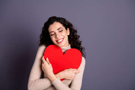 Close up photo beautiful she her lady overjoyed hands arms hold big large red paper heart form figure close chest invitation date prom wear casual pastel sweater pullover isolated grey backgroundの写真素材