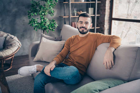 Portrait of his he nice-looking attractive bearded cheerful cheery content guy sitting on divan...
