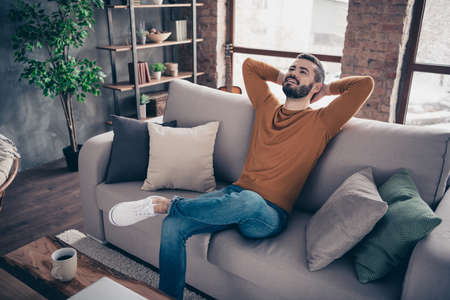 Portrait of his he nice attractive bearded cheerful cheery content guy sitting on divan having rest at industrial loft interior wooden brick style living-room indoorsの写真素材