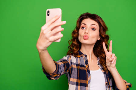 Close-up portrait of nice lovely sweet gorgeous attractive cheerful cheery positive wavy-haired girl in checked shirt taking selfie showing v-sign isolated over bright vivid shine green backgroundの写真素材