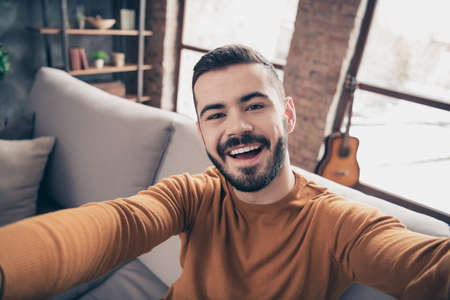 Close up photo of nice charming guy student hipster make photo moment toothy holidays weekends good-looking he his dressed orange sweater pullover big apartmentの写真素材