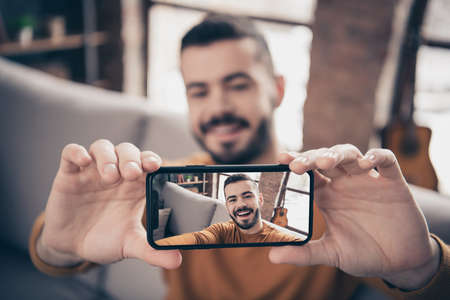 Close-up portrait of his he nice attractive cheerful cheery glad positive bearded guy taking making selfie holding camera in hands at industrial loft interior style living-roomの写真素材