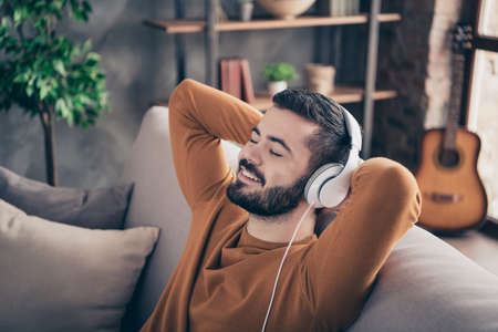Portrait of lovely sweet man touch head hand close eyes feel rejoice funny funky orange sweater pullover imagine soundtrack sound track sit divan comfy apartmentの写真素材