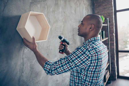 Profile side view photo of professional charming focused hold hand instrument hand work shelf expertise look dressed checked shirt plaid fashionable stand room apartmentの写真素材