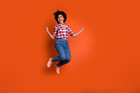 Full size photo of excited crazy jumping high lady yelling yeah raise fists wear jeans denim pants plaid shirt outfit isolated orange backgroundの写真素材
