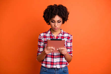 Portrait of nice cute attractive smart clever intellectual wavy-haired lady nerd wearing checked shirt reading news digital e-book isolated over bright vivid shine orange backgroundの写真素材