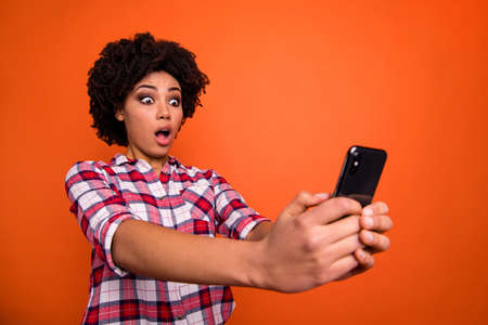 Close up photo of stupor model lady hold hands telephone reader email boss fired wear casual checkered plaid shirt isolated orange bright backgroundの写真素材