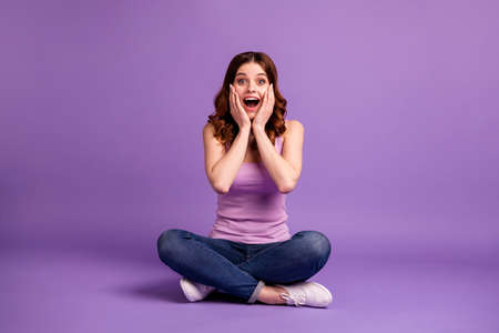 Portrait of cute teenager touch cheeks face palms hands scream shout wow, omg feel rejoice impressed astonished sit wear sneakers tank-top modern clothing isolated purple backgroundの写真素材