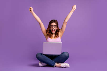 Portrait cheerful pretty trendy hipster youth modern technology sit legs crossed, folded denim jeans achievements aims celebrate isolated eyewear eyeglasses singlet tank-top purple violet backgroundの写真素材